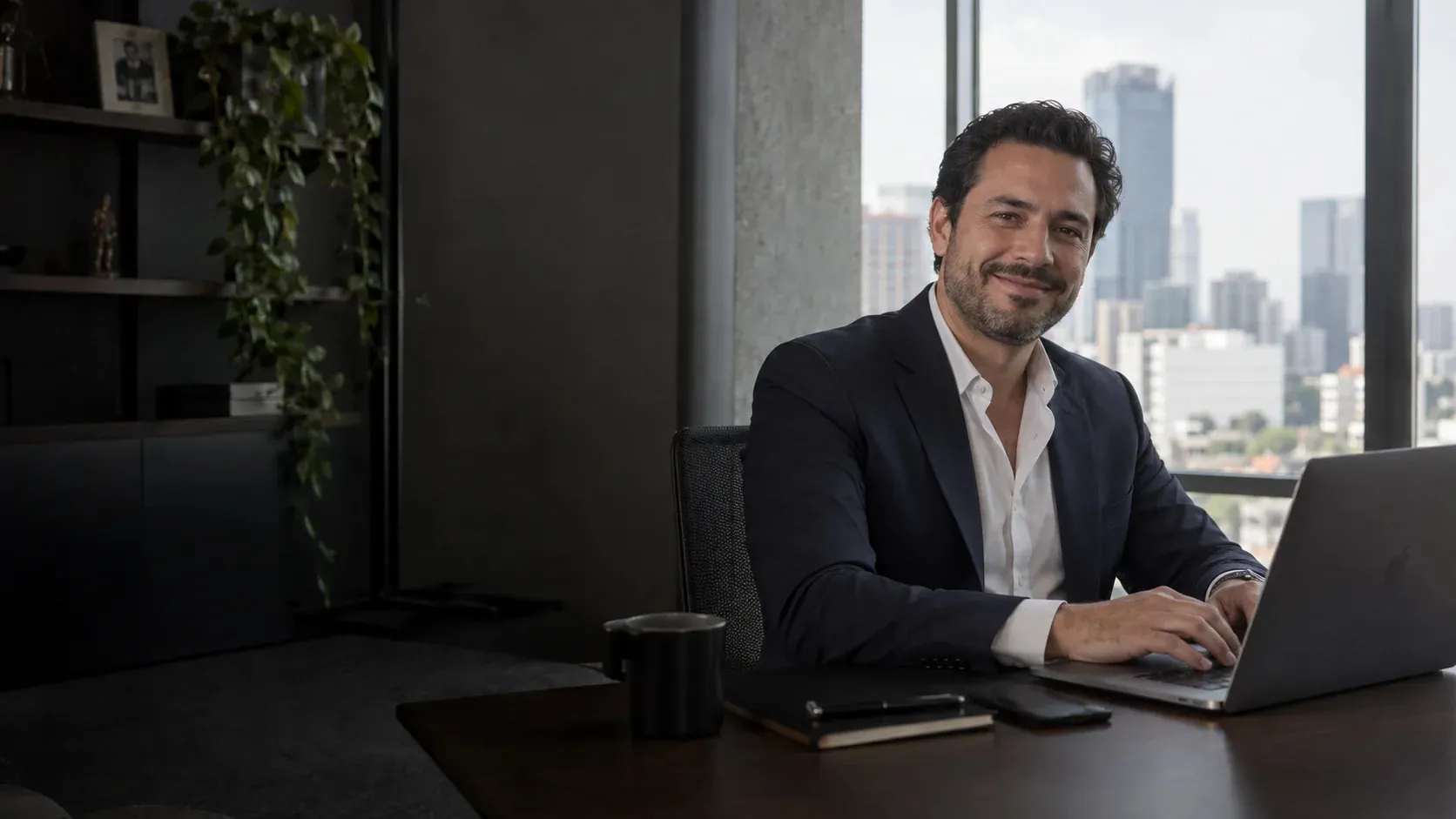 Empresario con traje sonriente sentado ante su computadora portátil